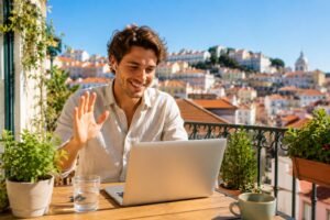 Jeune homme souriant en appel video sur un balcon ensoleille avec vue sur Lisbonne
